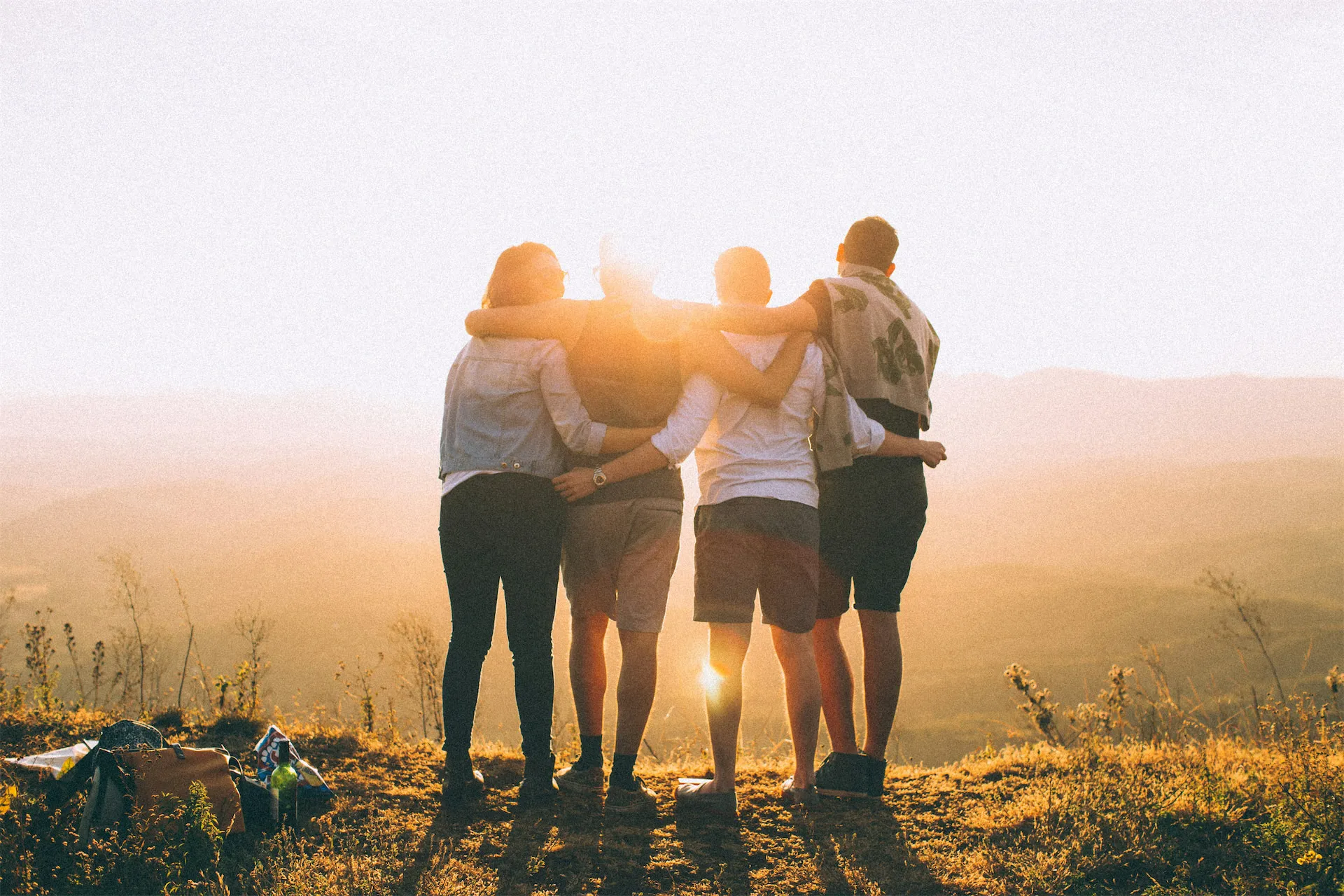 4 people with their arms over eachothers shoulders looking at the sunset